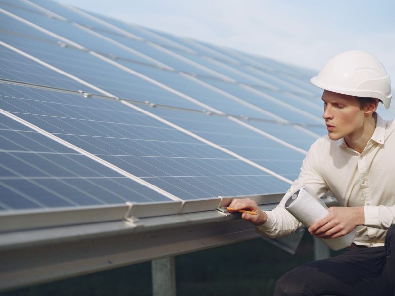Techniker mit Schutzhelm prüft eine Solarthermie-Anlage auf dem Dach