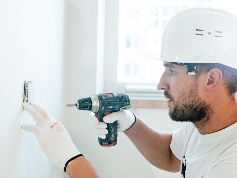 Handwerker mit Schutzhelm bohrt konzentriert eine Wandhalterung