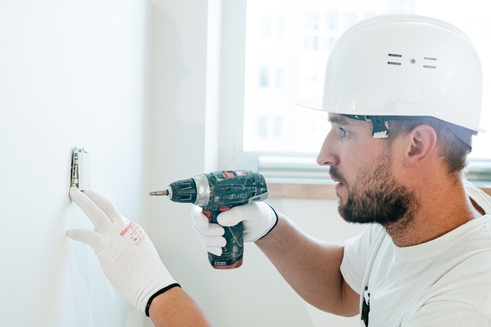 Handwerker mit Schutzhelm bohrt konzentriert eine Wandhalterung